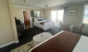 Hotel room with two neatly made beds, a round white ottoman, and a seating area by a sliding glass door to a balcony.